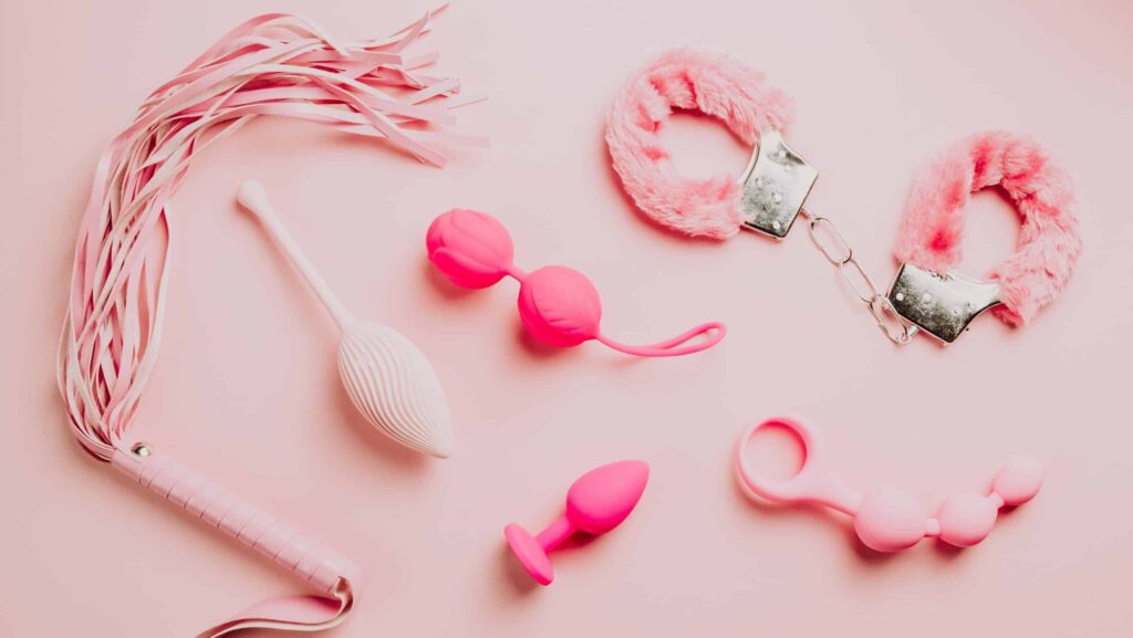 Pink and white adult intimacy accessories arranged on a pastel pink surface.